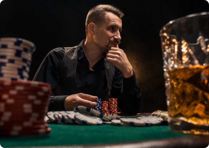 A man sitting at a poker table with chips and alcohol.