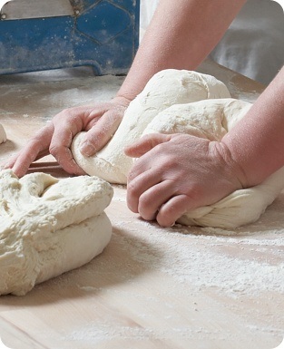 A person kneading dough on a wooden table.