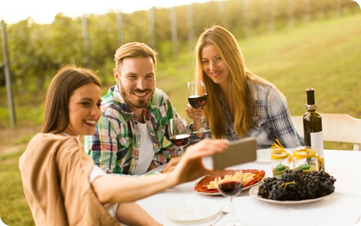 A group of people taking a selfie at a table with wine and food.