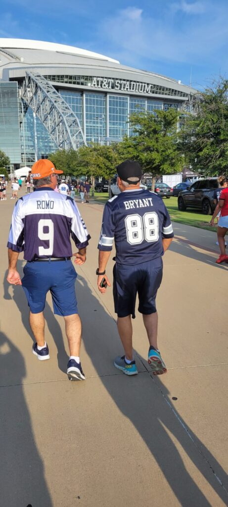 Two men walking in front of a stadium with cowboys jerseys.